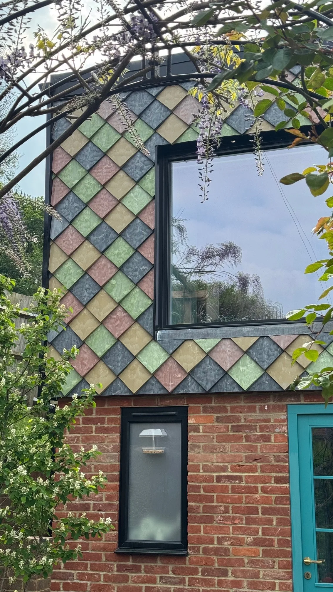 A two-storey extension clad with Pretty Plastic’s 100% recycled PVC tiles, with multiple windows framed by a vibrant mix of Terracotta, Green, Ochre and Grey – a striking example of circular façade design in contemporary architecture.