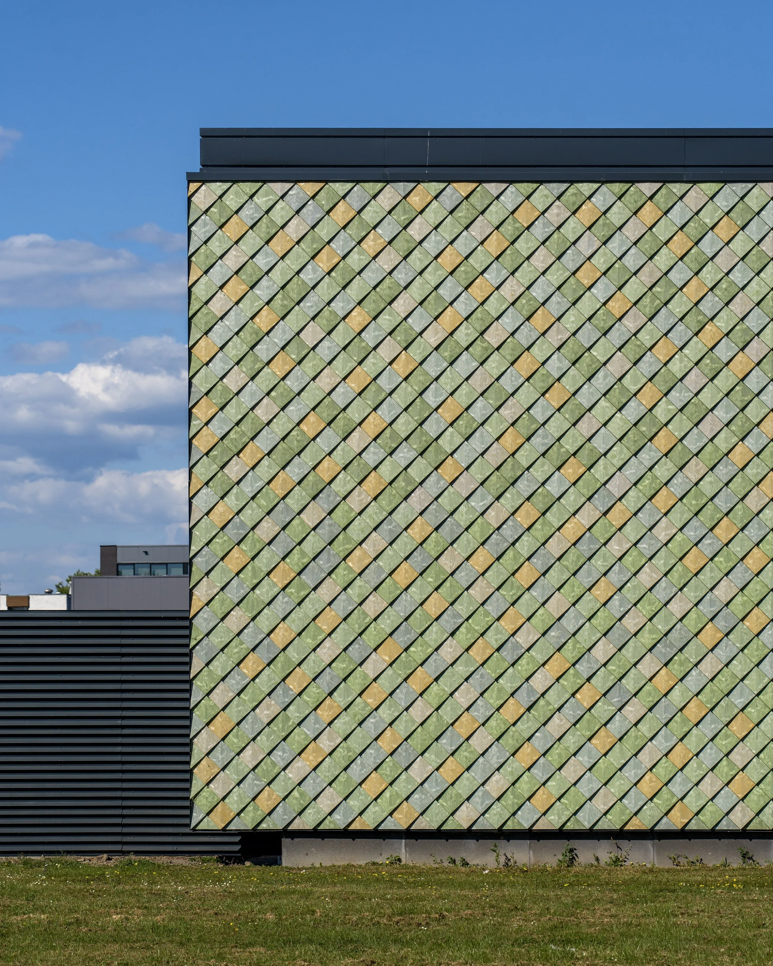 Corner view of the façade with vertical rhythm and layered texture – Pretty Plastic tiles in 4 shades.