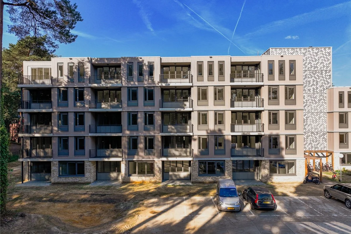 Aanschouw De Vijverhof in Berg en Dal vanaf de achterkant, waar het platte dak gekenmerkt wordt door de opvallende tegels van Pretty Plastic. Aan de rechterkant vind je ons project, geflankeerd door een modern appartementencomplex aan de linkerzijde.