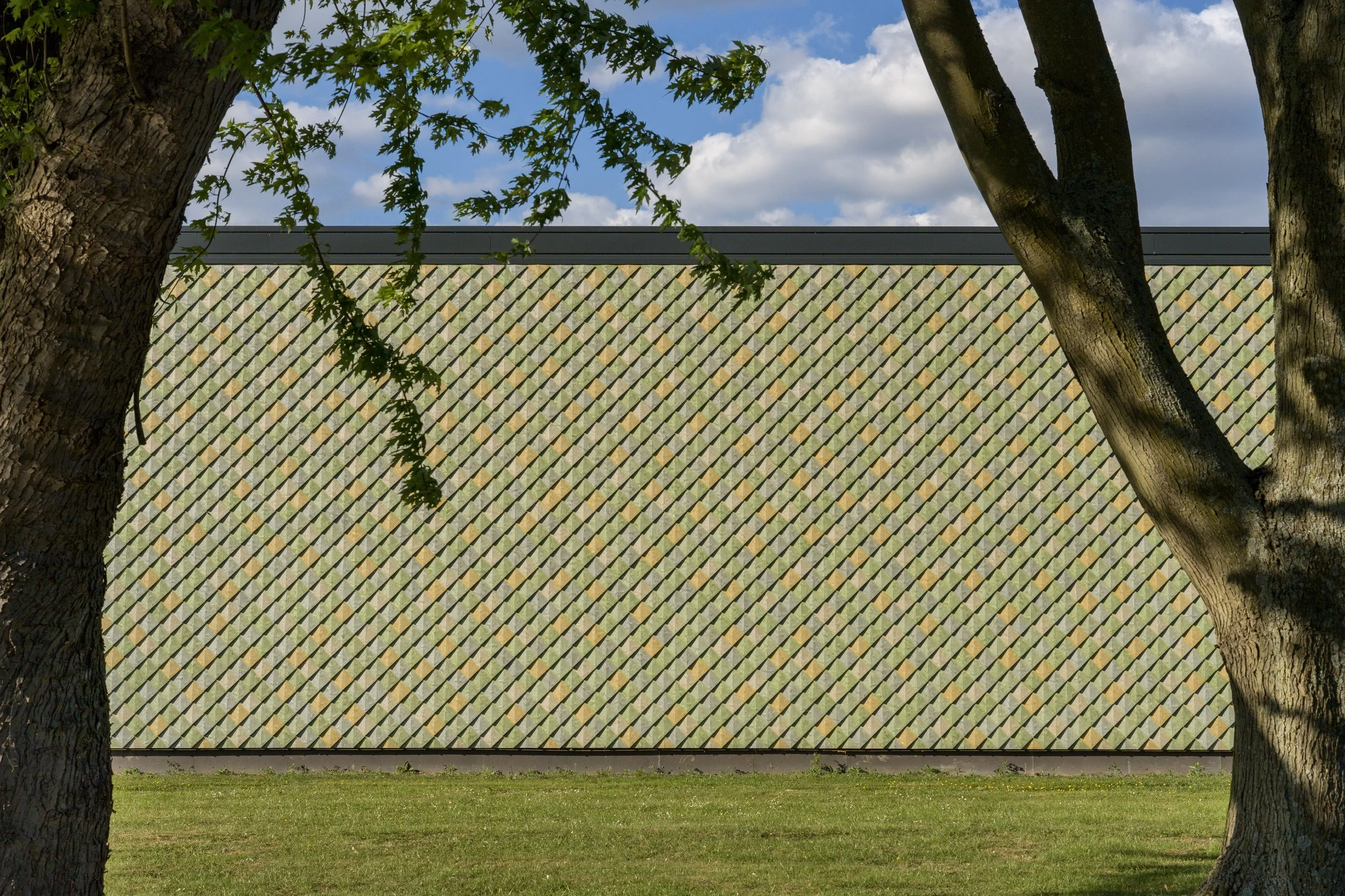 Side elevation of the Lensen Inspiration & Innovation Centre, Zaltbommel – Pretty Plastic First One tiles in green and ochre tones, with trees framing the recycled façade.