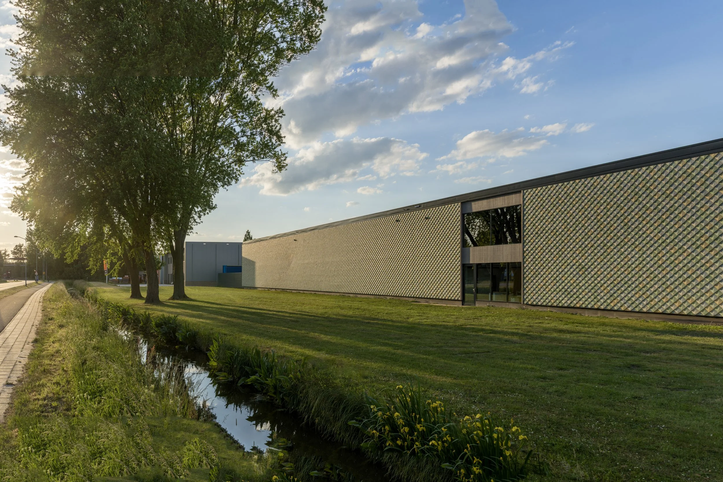 Side façade of Lensen Inspiration & Innovation Centre in Zaltbommel, featuring Pretty Plastic First One tiles in green and ochre.
