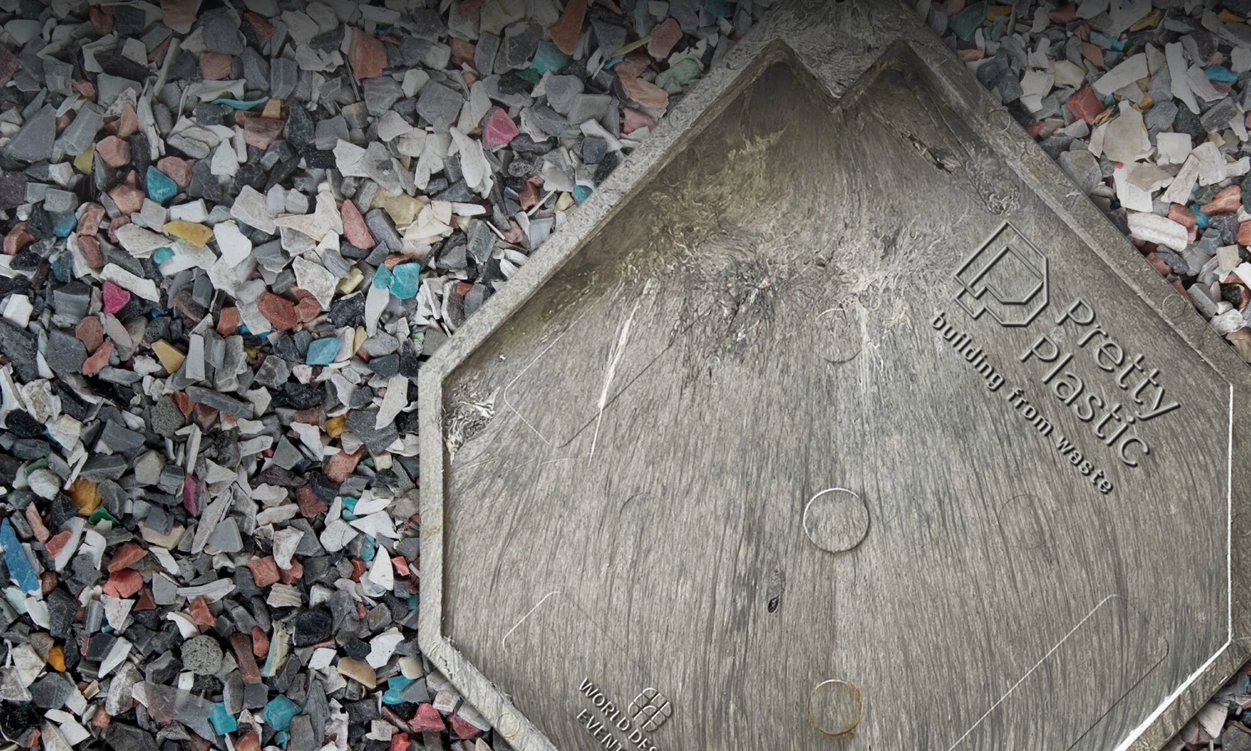 A metal plaque embedded in a concrete surface next to small, multicolored gravel stones.