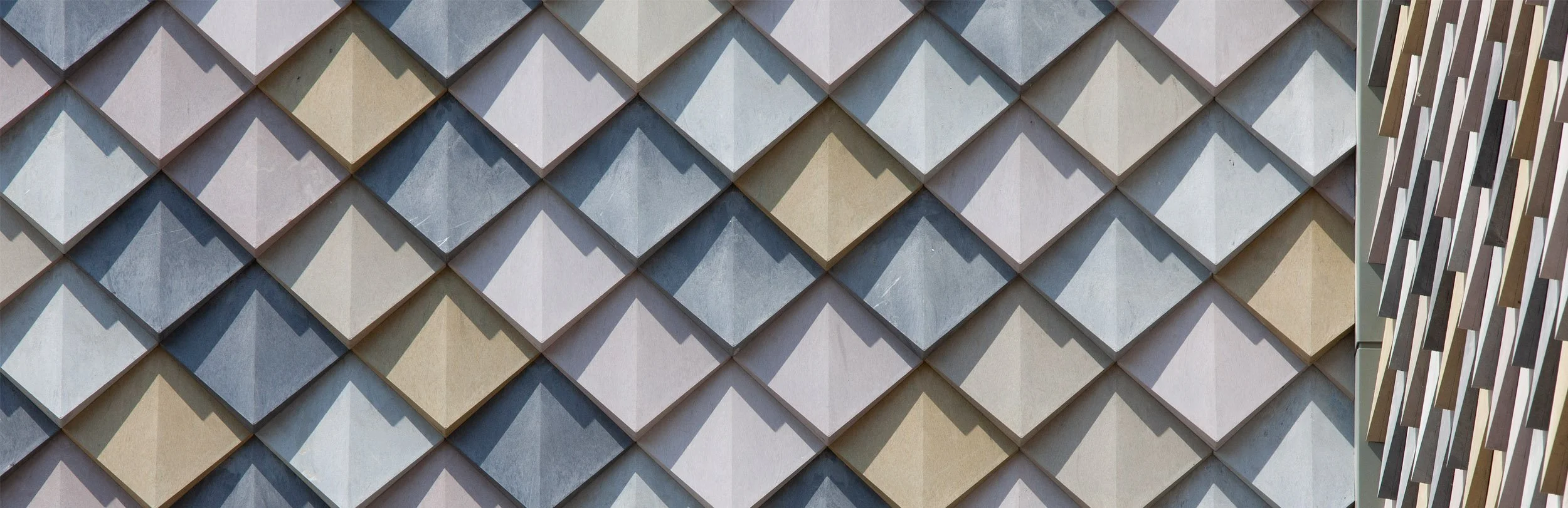 Close-up of a building facade with multicolored diamond-shaped tiles and a partial view of a wooden balcony railing.