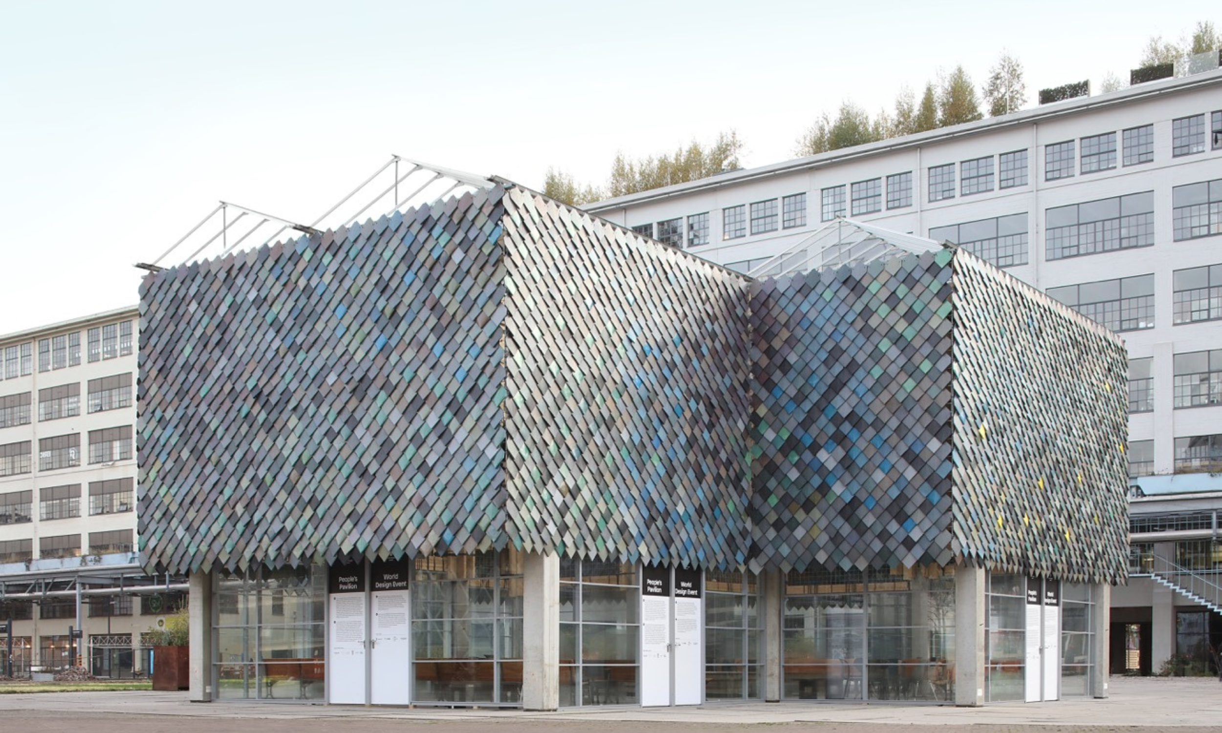 This photo provides a panoramic view of The People's Pavilion, epitomizing circular innovation and sustainability. With its facade shining in a rich palette of colors, all derived from recycled materials, and its roof and windows adorned with other c